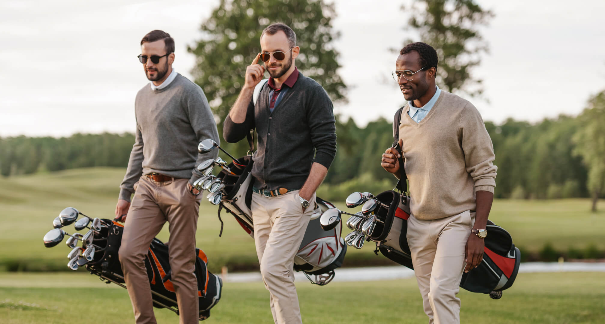 drei Personen beim Golfen mit Sonnenbrillen und Golftaschen